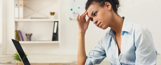 A woman is focused on her computer screen with a pair of eyeglasses placed next to her