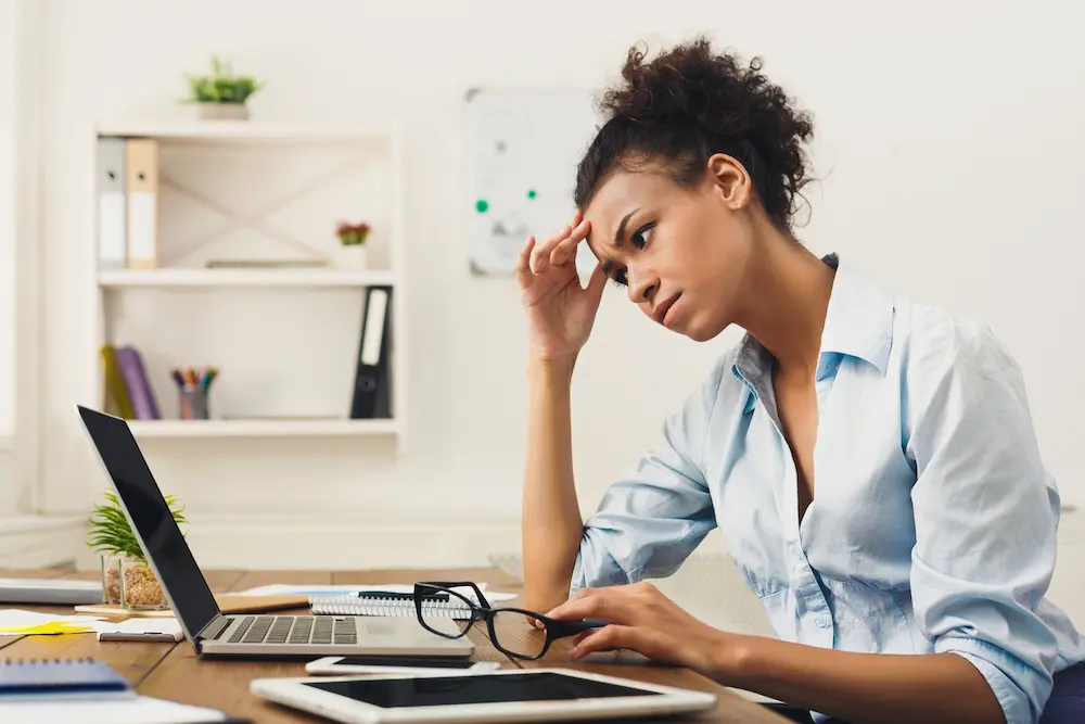 A woman is focused on her computer screen with a pair of eyeglasses placed next to her