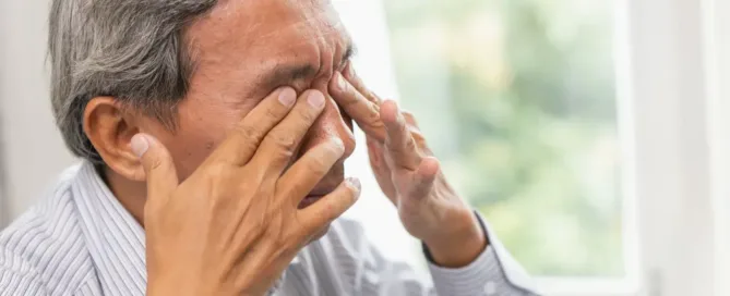 A man with a tired expression gently rubbing his eyes, indicating fatigue from prolonged screen time, while seated in a casual indoor setting