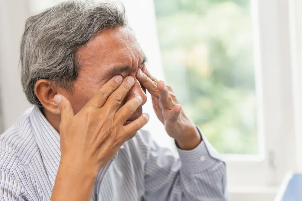 A man with a tired expression gently rubbing his eyes, indicating fatigue from prolonged screen time, while seated in a casual indoor setting