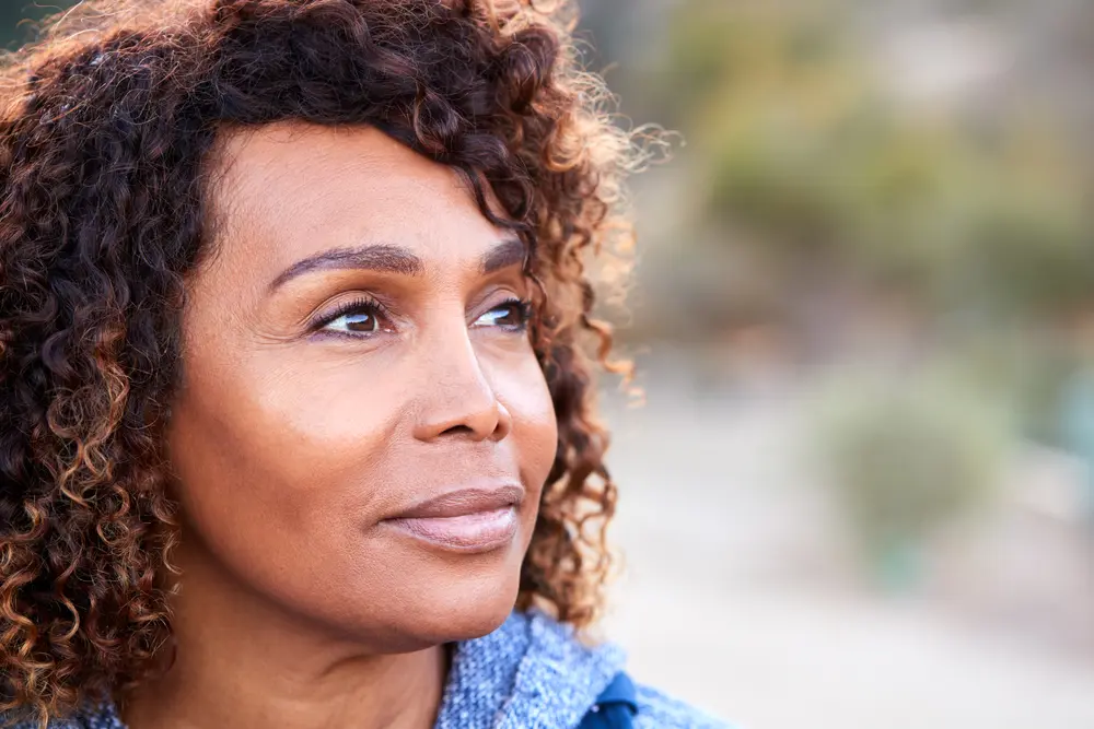 A woman gazing thoughtfully into the distance while outdoors, with a serene expression, surrounded by nature