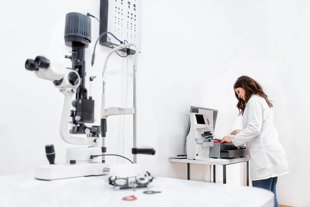 A healthcare worker organizes and sets up various eye examination tools and equipment in preparation for patient assessments in an ophthalmology setting