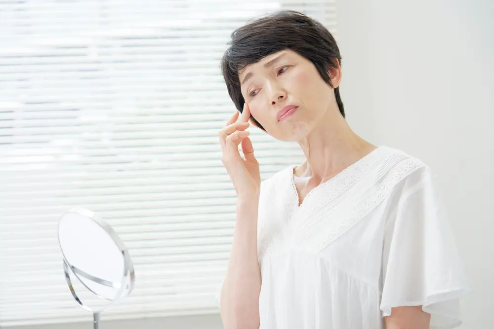 A woman has a small mirror close to her face, with her finger near her eye as if adjusting or examining something related to her vision or eye are