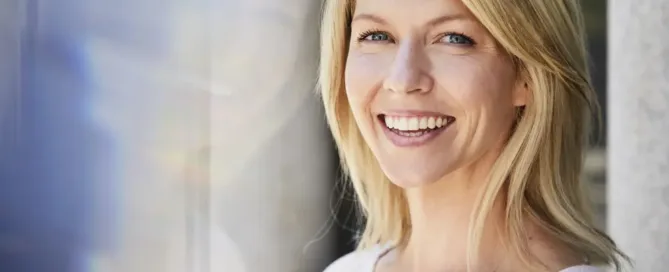 A woman with a joyful expression, casually smiling in a bright, outdoor setting